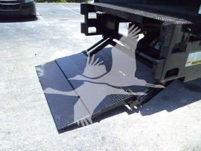 Truck ramp/underbody of a 2019 International Durastar 4300 with a lowered metal loading ramp showing a textured diamond plate. Some labels visible on the frame.