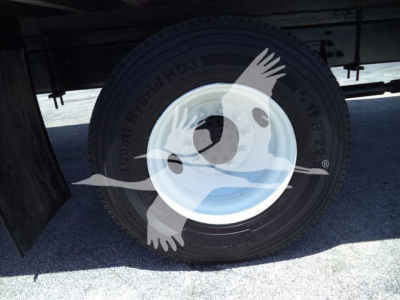 Truck tire and wheel under a box truck showing a rugged tire with white rim and sidewall labels.