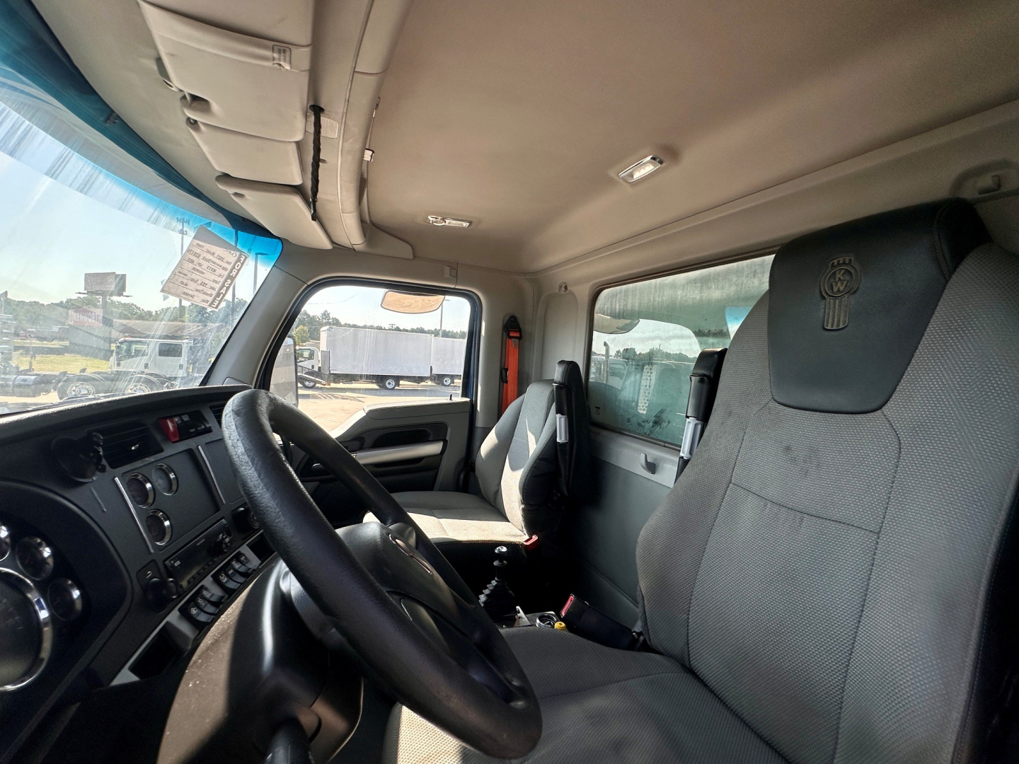 Truck cab interior showing steering wheel, dashboard, and gray fabric seats in a 2021 Kenworth T880 with overhead storage.