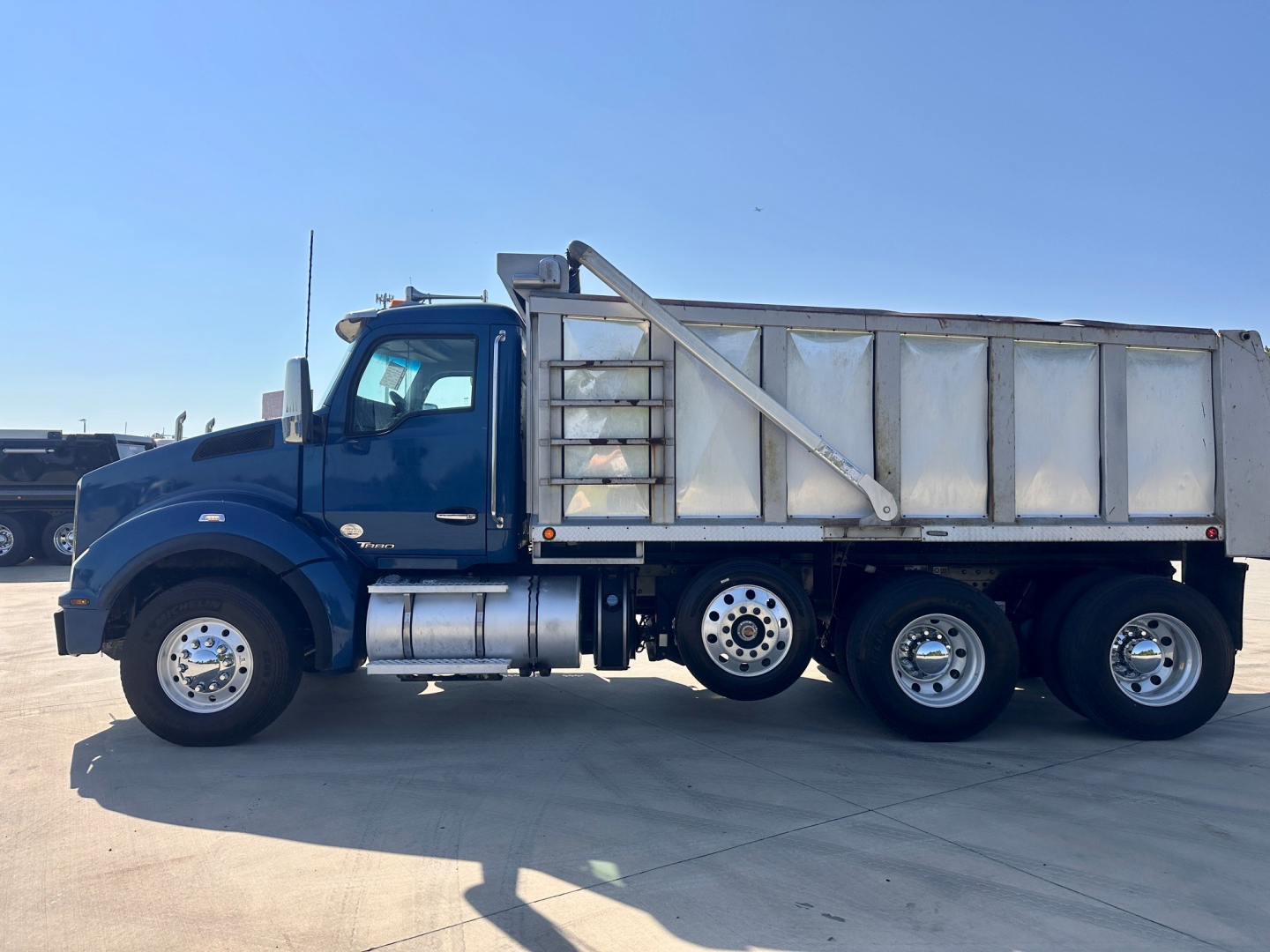 Kenworth T880 dump truck side view showing cab, fuel tanks, and large aluminum dump body.