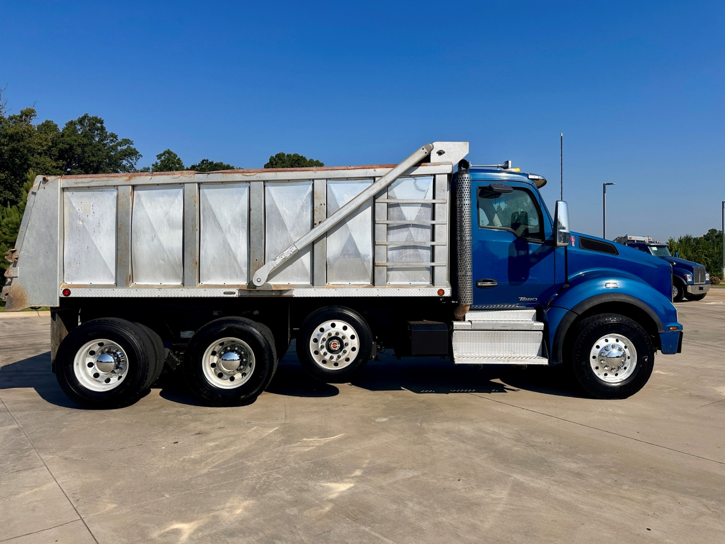 Kenworth T880 dump truck side view in blue cab with silver dump body and side rails.