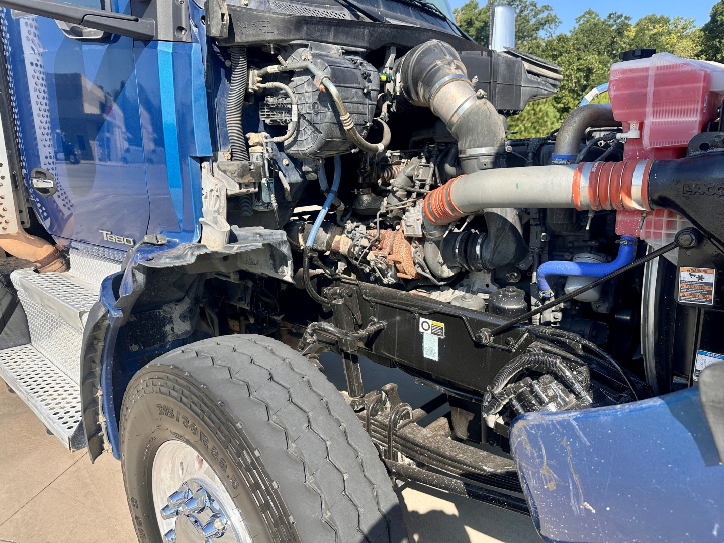 Kenworth T880 engine bay with visible turbocharger, hoses, and radiator components in a blue truck cab; intake and exhaust plumbing partially exposed.