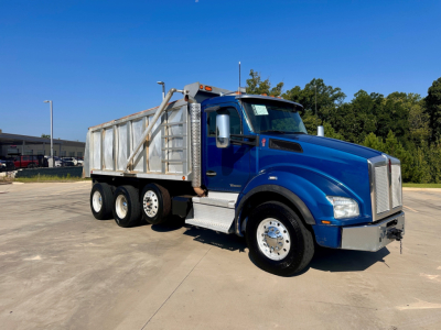 Blue Kenworth T880 dump truck with silver dump bed, side view showing front grille and dual rear axles.