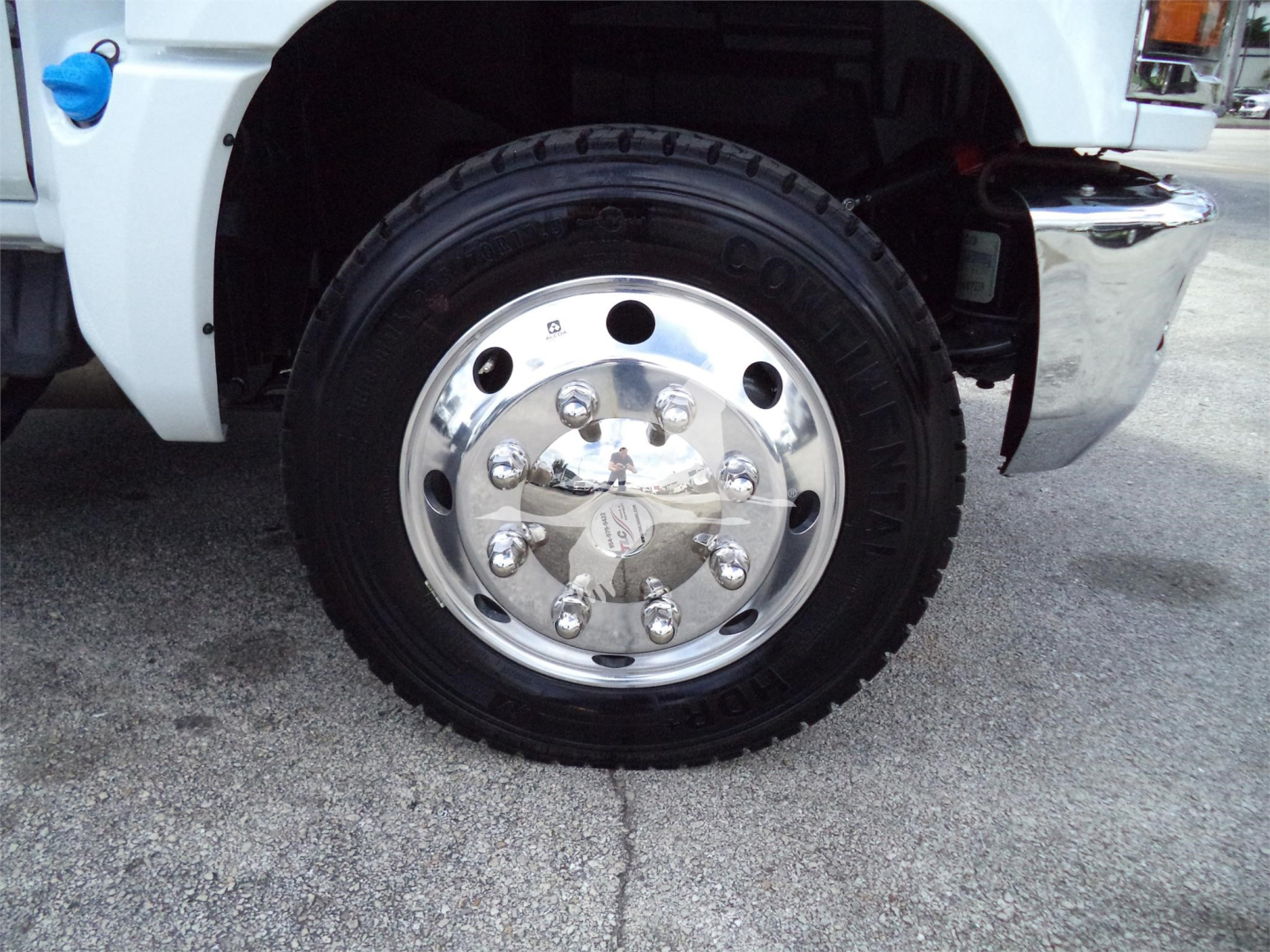 Front wheel of a white 2023 Chevrolet Silverado 6500HD rollback truck showing chrome wheel with lug nuts and Goodyear tire.