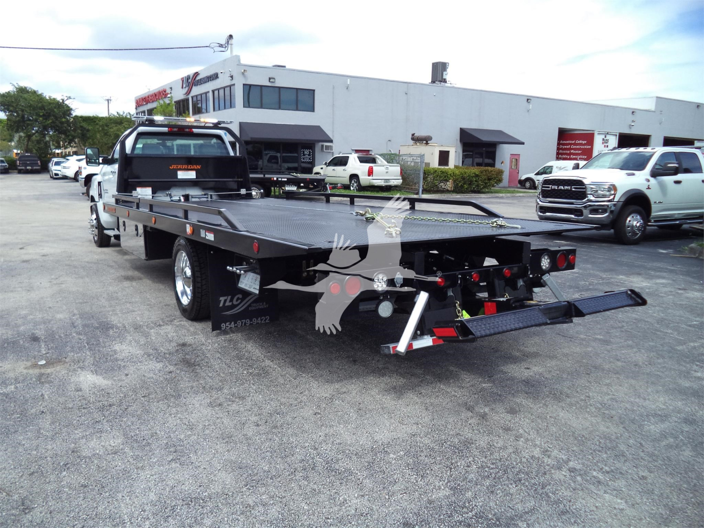 Back-view of a Silverado 6500HD rollback tow truck with flatbed and ramp in a dealership lot.