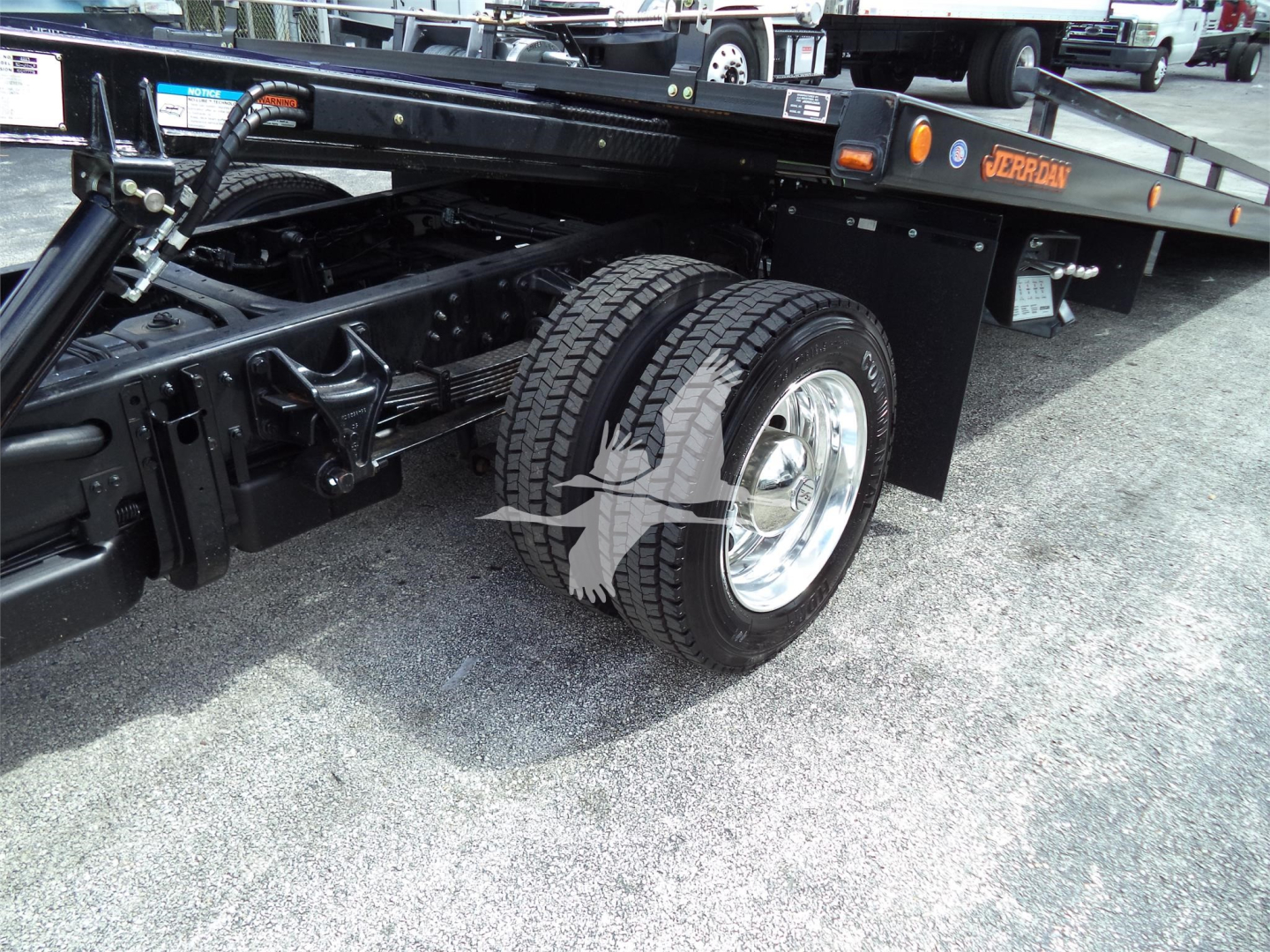 Truck chassis and dual rear wheels of a rollback w/ black frame and orange lettering reading JERRDAN on the bed.