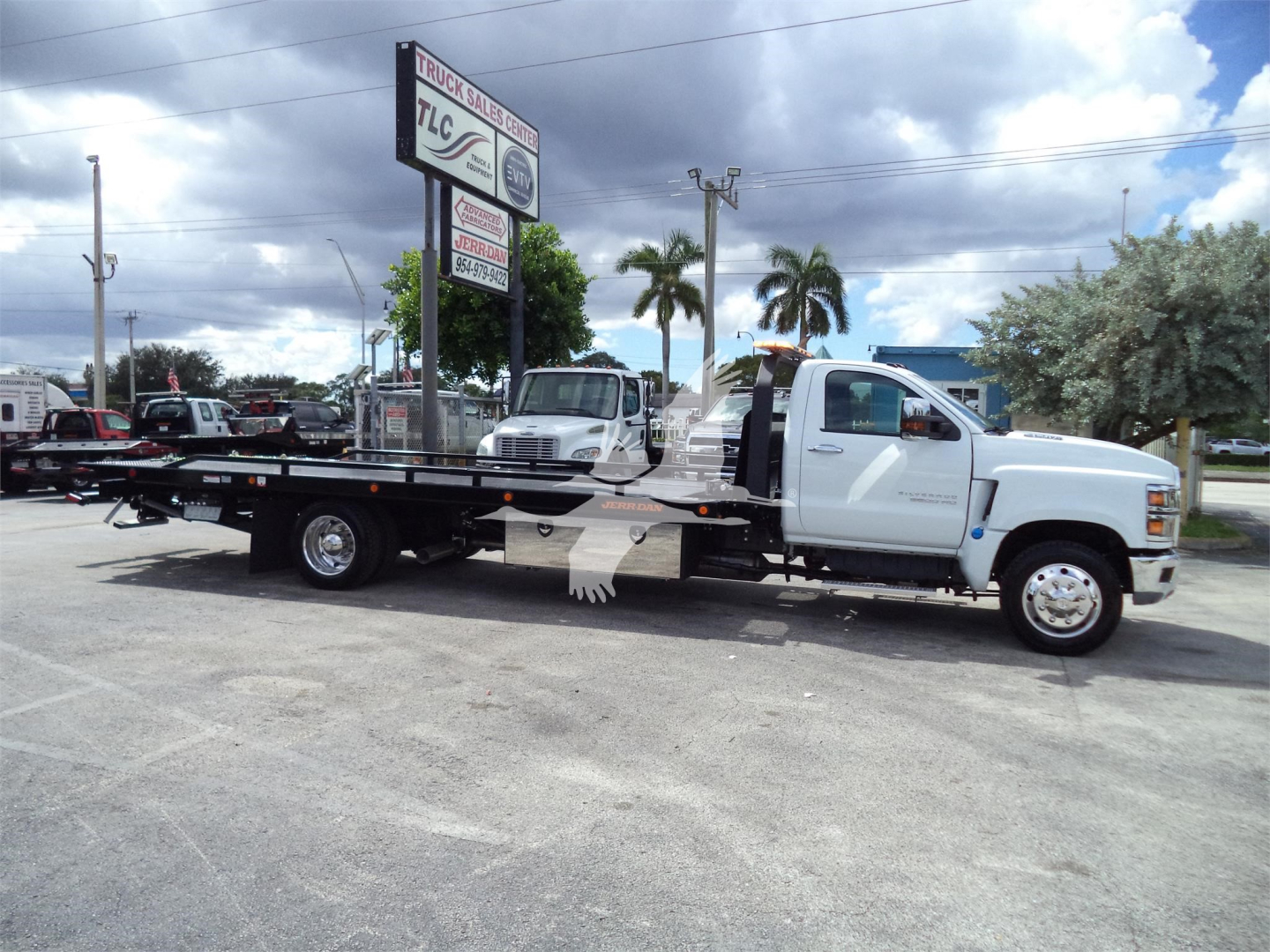 Truck: 2023 Chevrolet Silverado 6500HD rollback tow truck with long flatbed and white cab, side view.