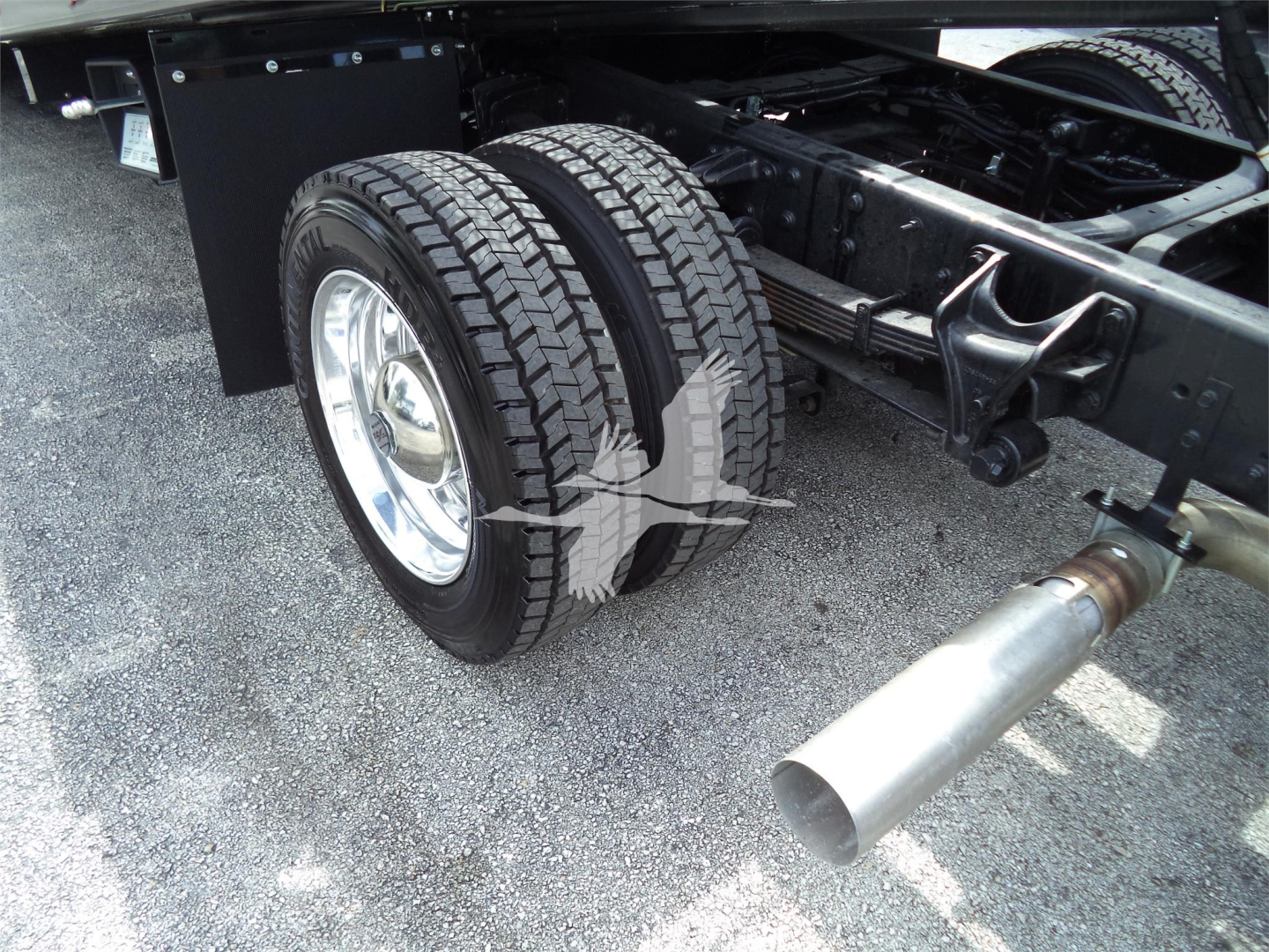 Truck rear dual tires and exhaust visible under chassis of a 2023 Chevrolet Silverado 6500HD rollback truck showing dual rear wheels and large exhaust tip.