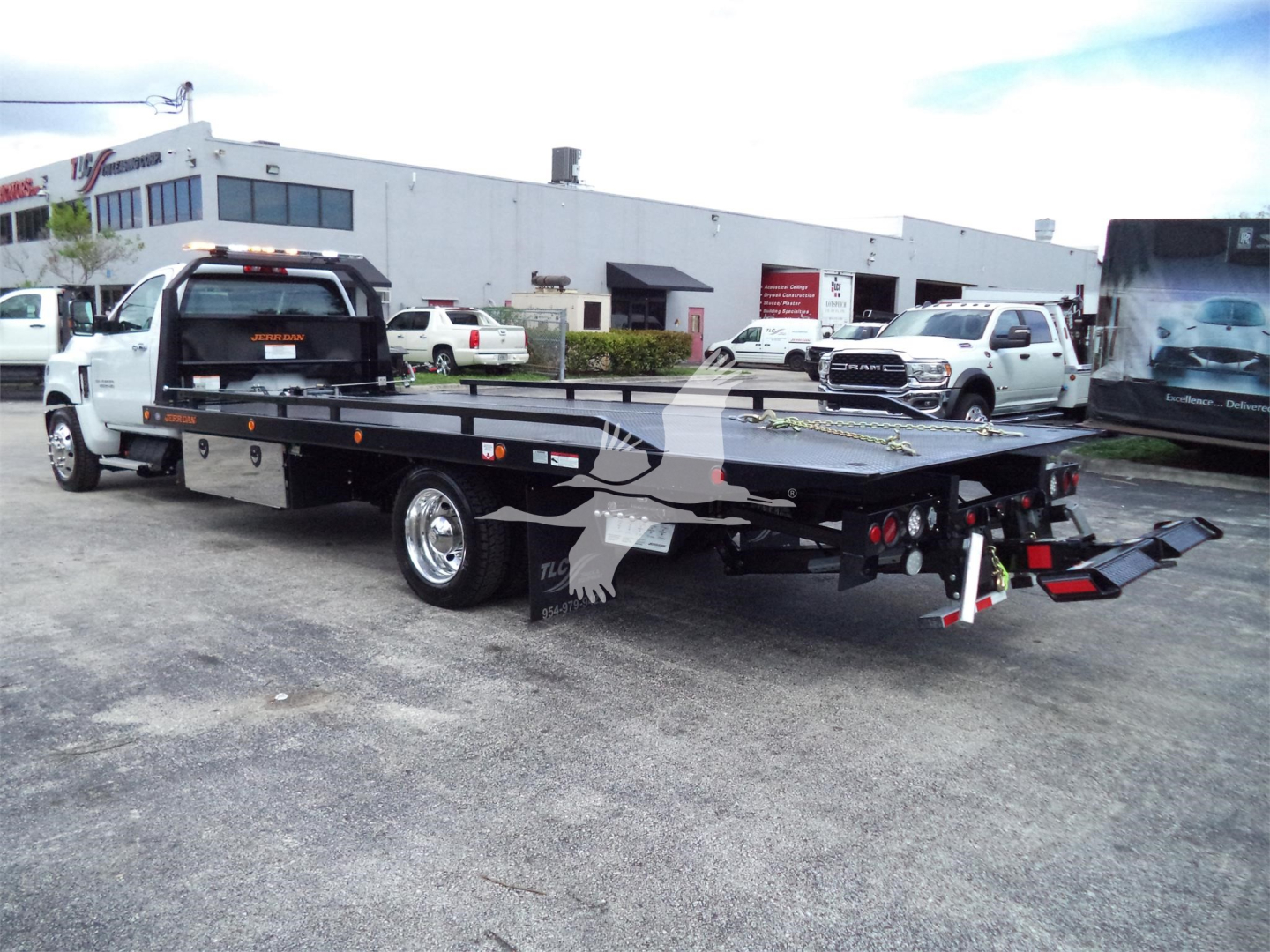 Flatbed tow truck in a dealership lot with a Chevrolet Silverado 6500HD roll-back; visible text includes stock numbers and dealership signage in background.