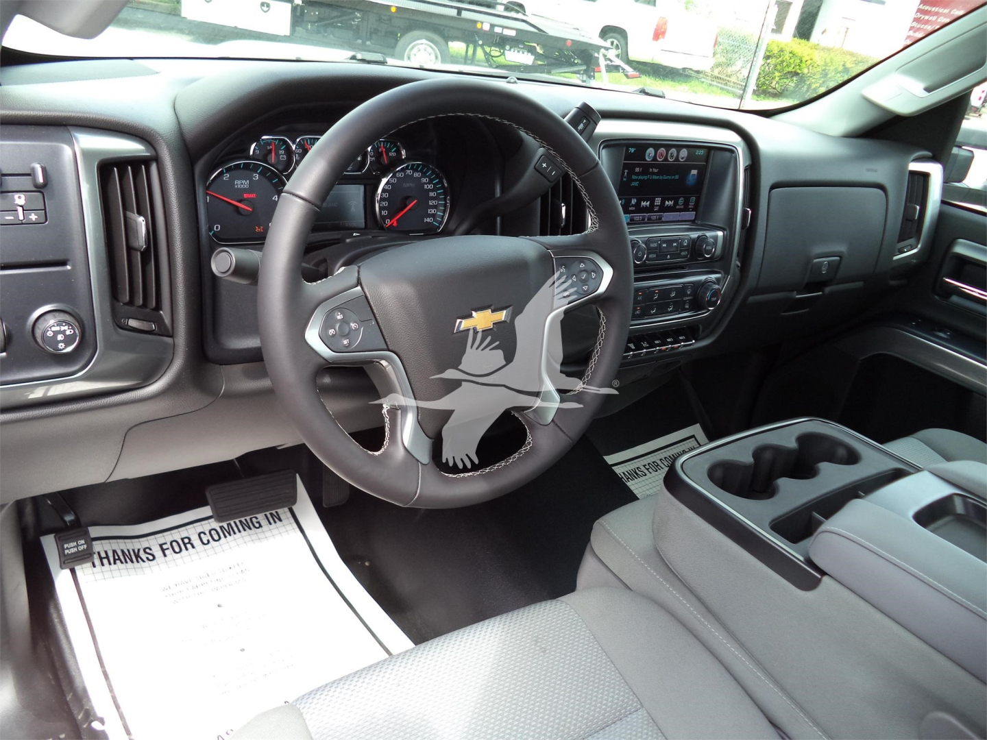 Truck interior showing steering wheel with Chevrolet emblem, dashboard with gauges, touchscreen display, center console with cup holders, and floor mats.