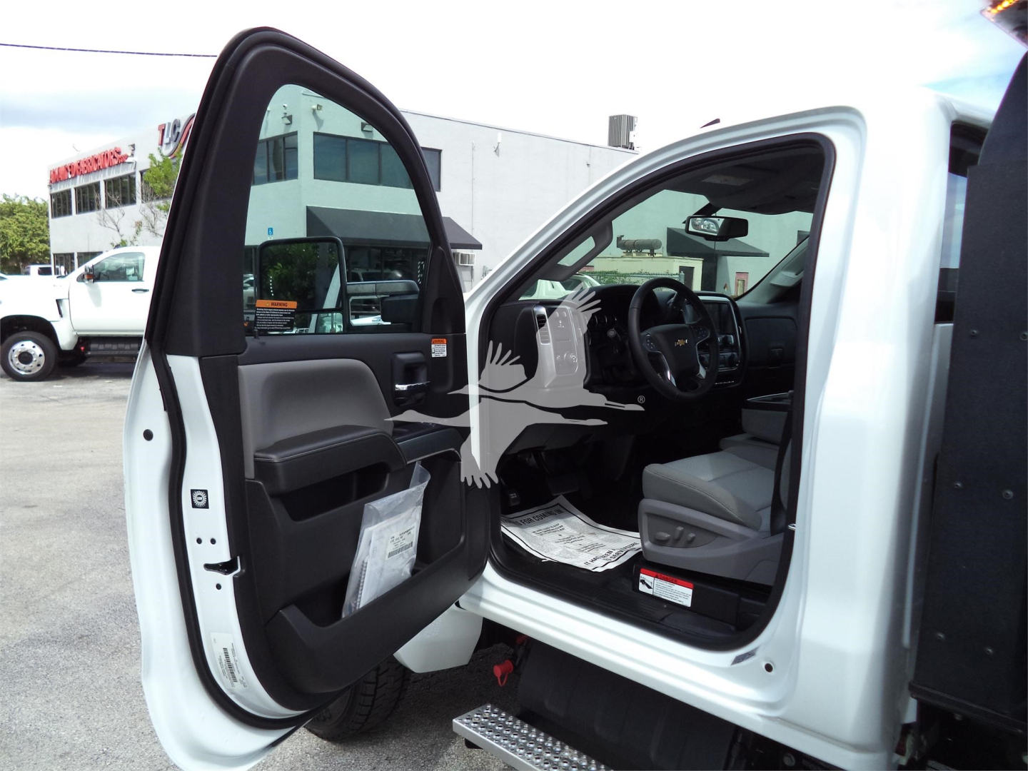 Truck cab interior open door showing dashboard and driver seat with papers on floor and exterior white body panels.