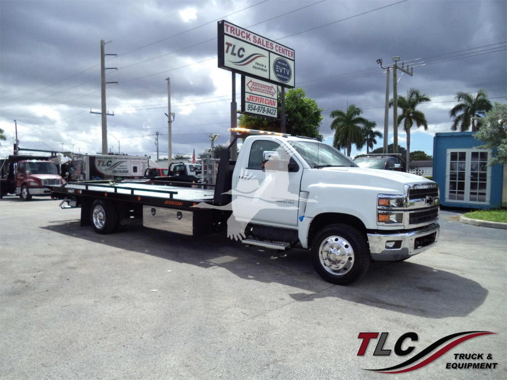 Truck in a dealership lot: 2023 Chevrolet Silverado 6500HD rollback tow truck with TLC Truck Sales Center signage in background. Visible text includes VIN 1HTKHPVM9PH768760 and stock number J68760 on a sign.