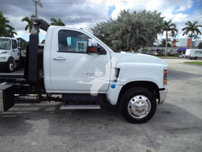 Truck side view of a 2023 Chevrolet Silverado 6500HD rollback with white cab, chrome wheel, and hydraulic lift undercarriage.