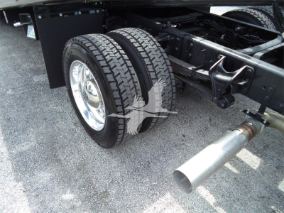 Truck rear dual tires and exhaust visible under chassis of a 2023 Chevrolet Silverado 6500HD rollback truck showing dual rear wheels and large exhaust tip.
