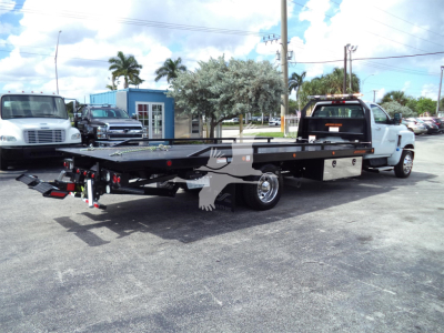 Truck bed tow rollback equipment on a white Chevrolet Silverado 6500HD with extended flatbed trailer in a dealership lot, rear view showing hitch and lights.