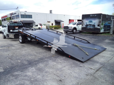 Flatbed tow truck with a long black steel ramp bed and tiedowns, in a dealership lot.