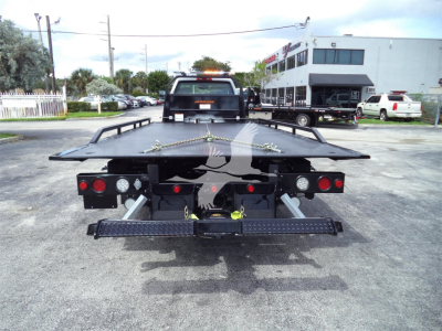 Flatbed tow truck rear view showing Chevrolet Silverado 6500HD near an auto lot.