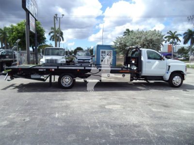 Flatbed tow truck side view showing Silverado 6500HD chassis with long flatbed and white cab, VIN plate area not legible.