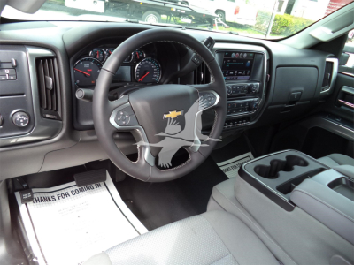 Truck interior showing steering wheel with Chevrolet emblem, dashboard with gauges, touchscreen display, center console with cup holders, and floor mats.