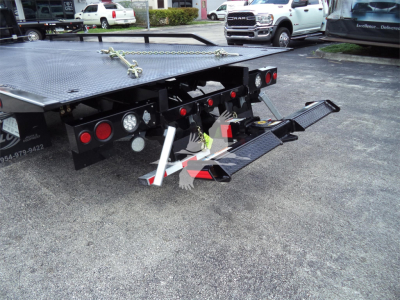 Flatbed tow truck equipment showing rear of rollback bed with hydraulic ramps and taillights.