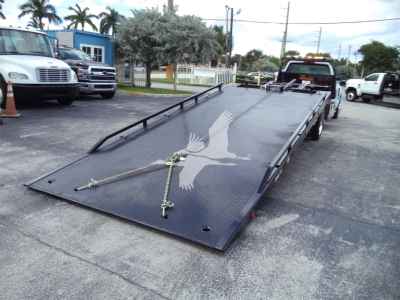 Truck bed of a 2023 Chevrolet Silverado 6500HD rollback with a lowered flatbed and ramp; visible chain tie-downs and a gull icon graphic on the deck.