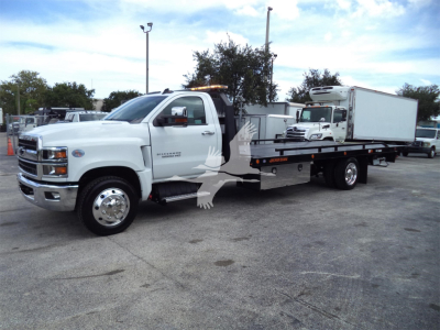 White 2023 Chevrolet Silverado 6500HD rollback tow truck with extended flatbed and cab, side view showing chrome wheel covers and rear equipment.