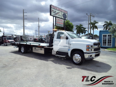 Truck in a dealership lot: 2023 Chevrolet Silverado 6500HD rollback tow truck with TLC Truck Sales Center signage in background. Visible text includes VIN 1HTKHPVM9PH768760 and stock number J68760 on a sign.