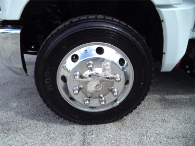 Truck wheel close-up showing chrome steel hubcap with lug nuts and Hankook tire on white Chevrolet Silverado 6500HD rollback truck.