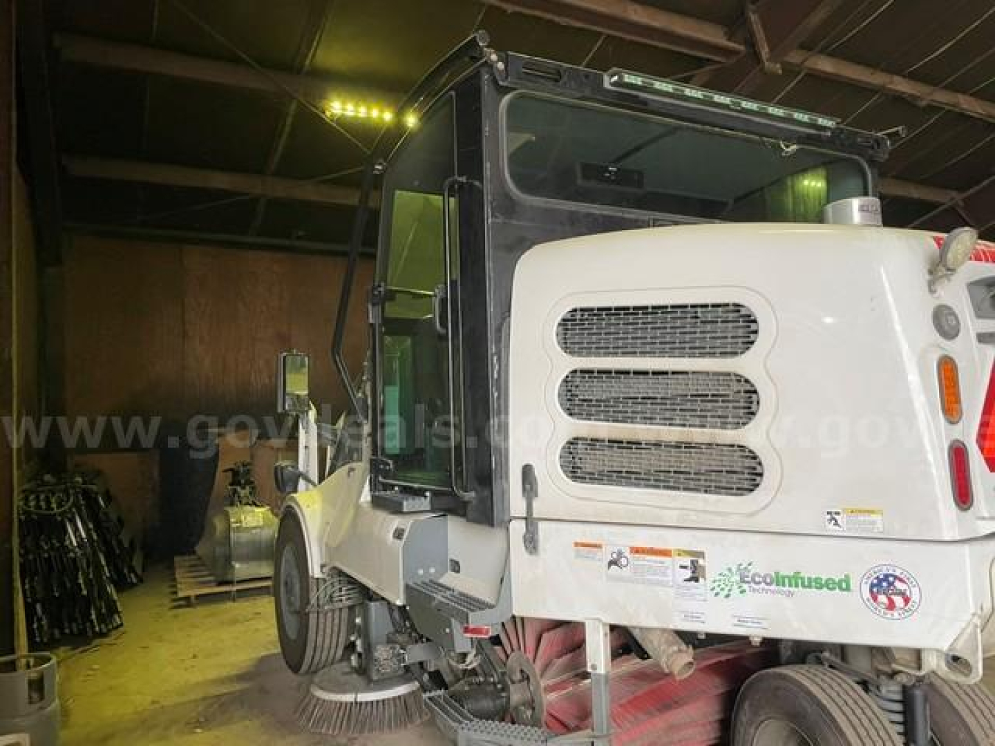 Elgin Pelican sweeper truck side view showing white cab and engine compartment with black grille and stickers