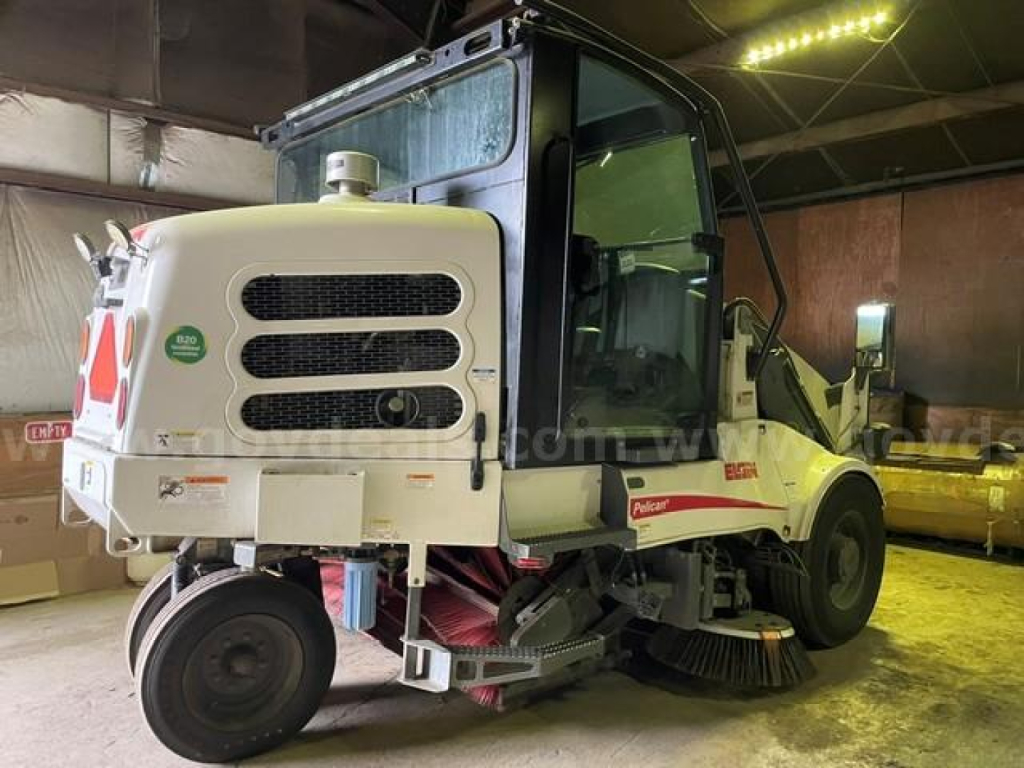 Elgin Pelican sweeper truck in an indoor lot showing front and side view with sweeping brushes and cabin label