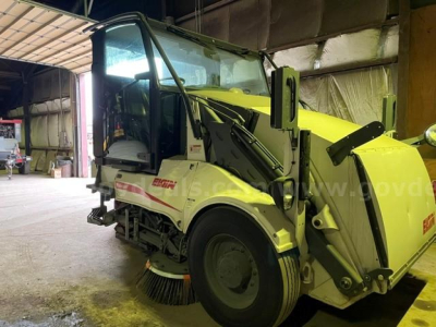 Elgin Pelican street sweeper in a warehouse, side view showing front brushes and yellow body with white cab, stock number 2631-1915.