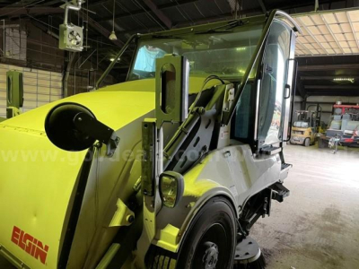 Elgin Pelican sweeper truck in a warehouse setting showing cab and front scoop with Elgin branding