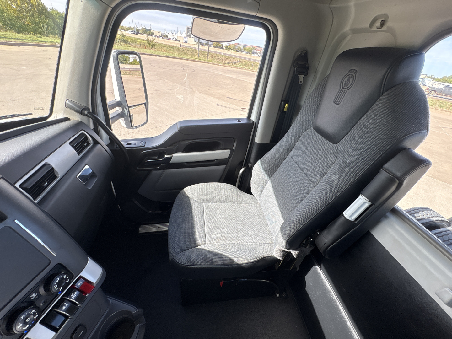 Kenworth T880 cabin interior showing driver's seat and dashboard with window and side mirror.