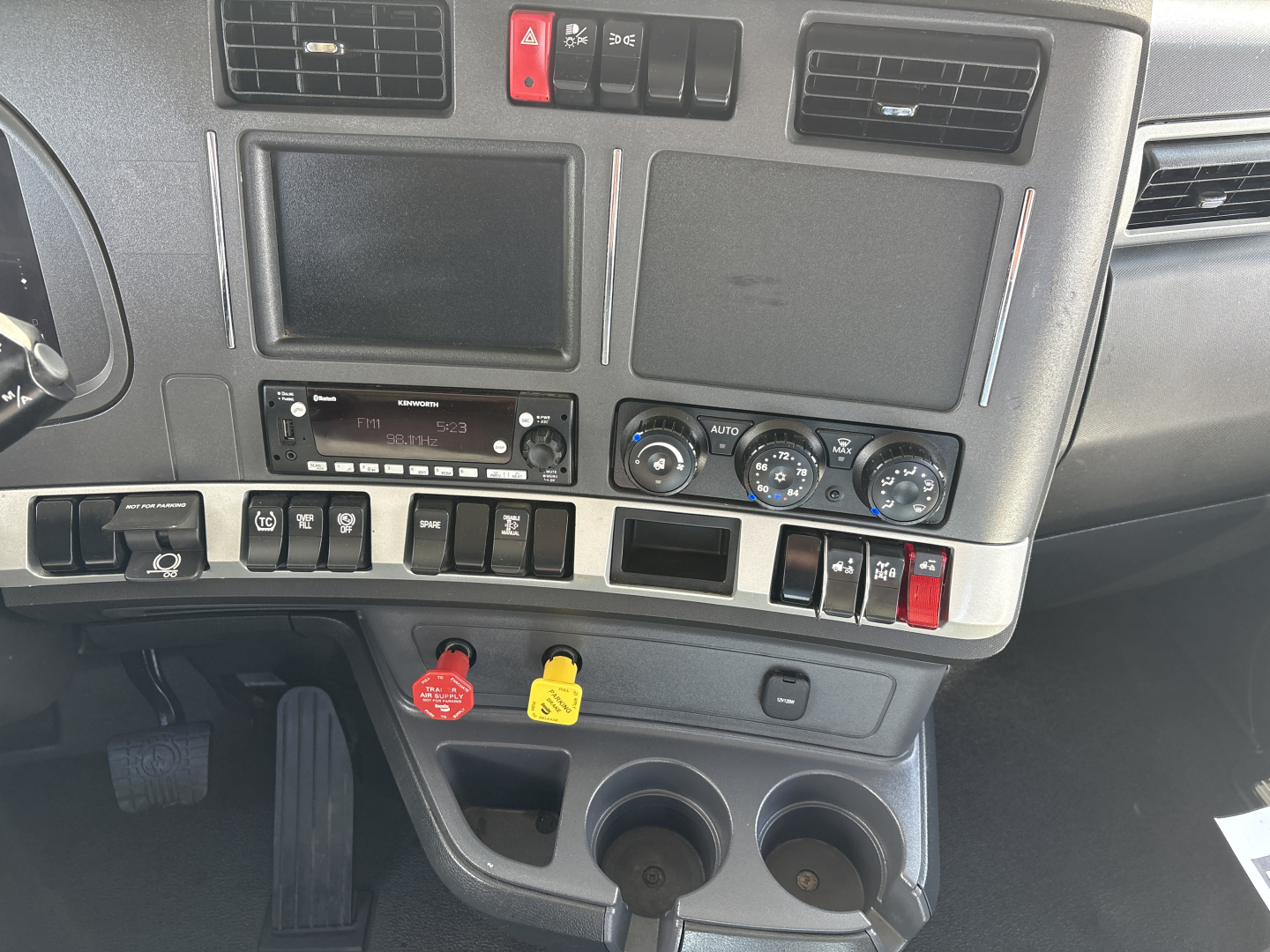 Kenworth T880 dash controls showing ignition switches, climate knobs, cup holders, and empty slots.