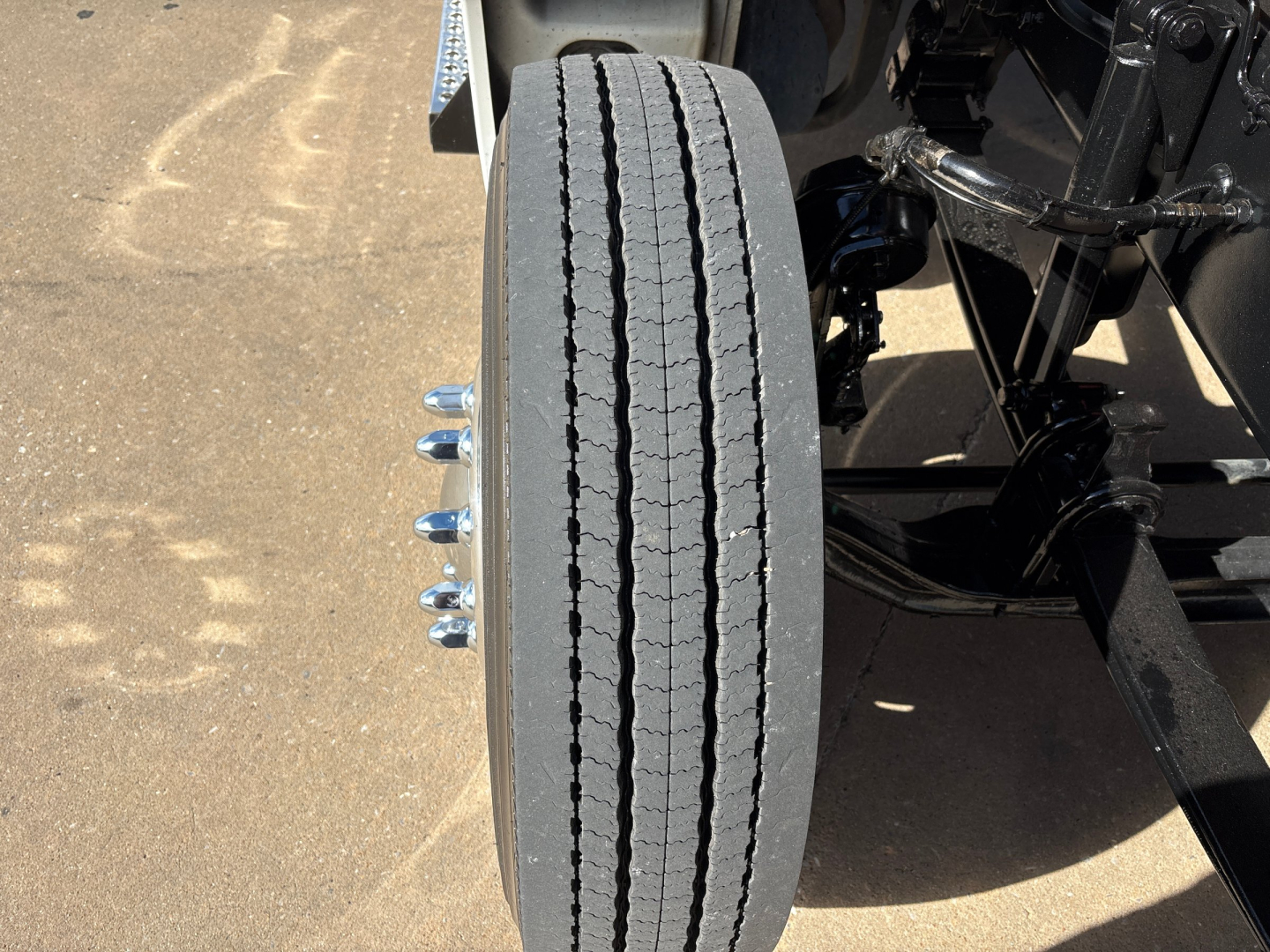 Kenworth T880 front wheel and suspension showing vertical twin exhaust? Wait, image shows a single tire with dual tandem axle components and suspension arms in a truck chassis.