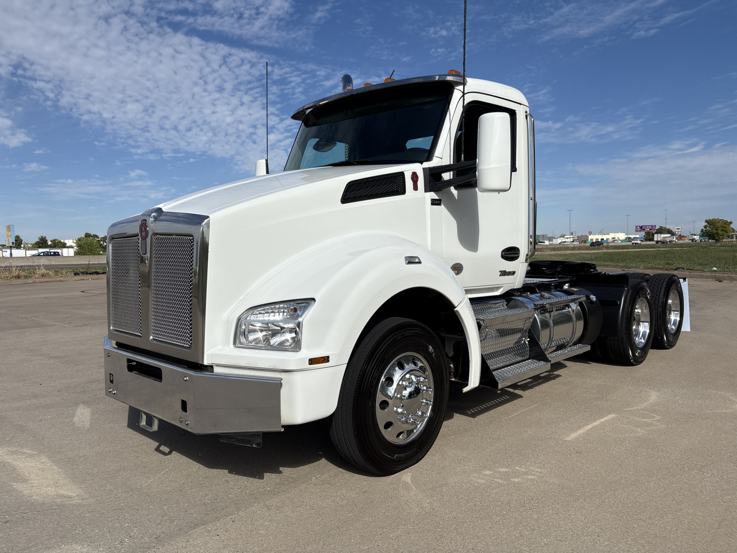 Kenworth T880 conventional daycab truck in white, front three-quarter view, with chrome grille, large bumper, and dual rear axles. No visible text on components.