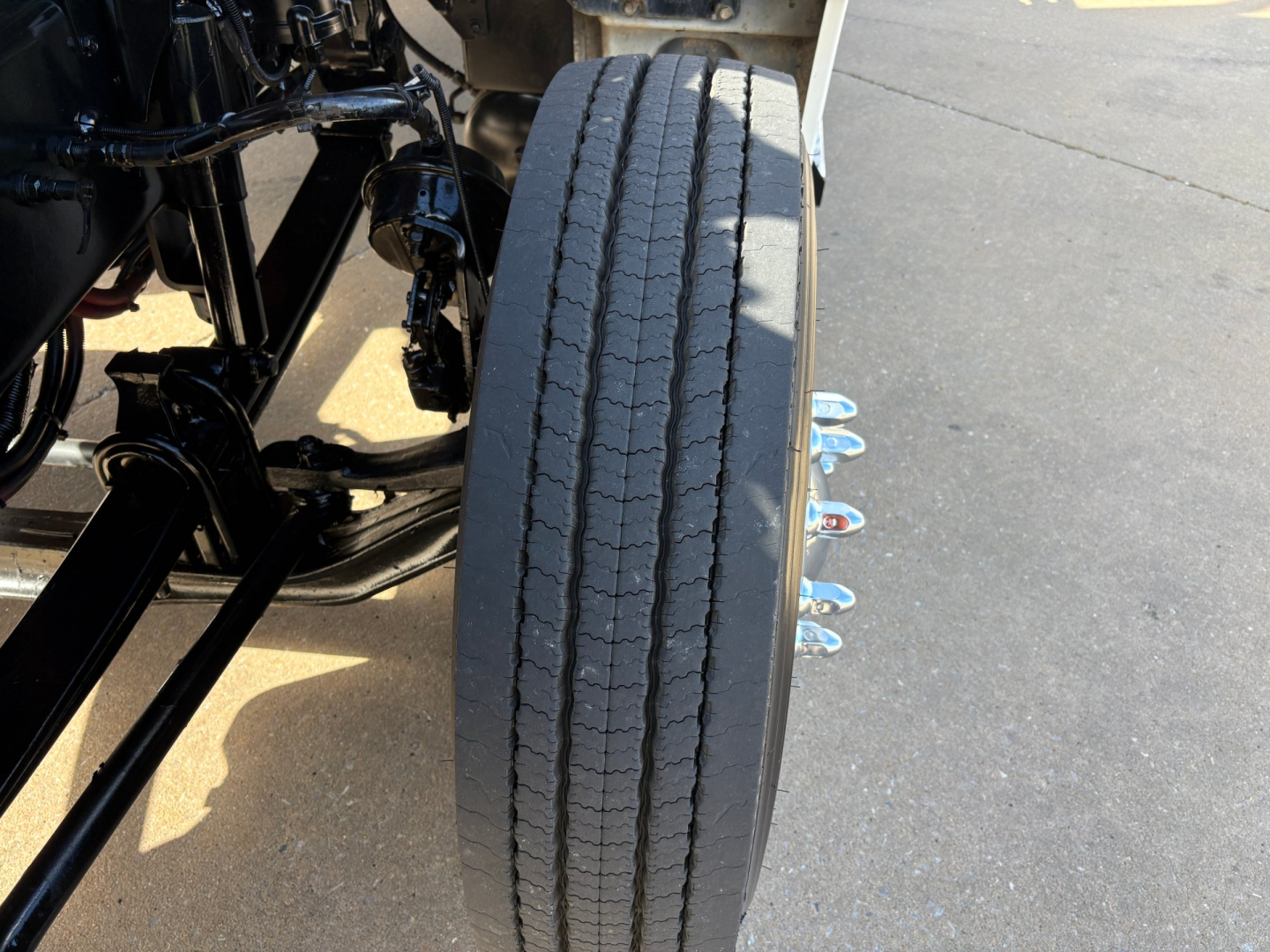 Kenworth T880 wheel and chassis with dual rear axles and tire tread visible; front side shows drive line and suspension components.