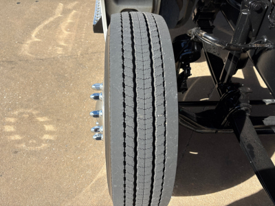 Kenworth T880 front wheel and suspension showing vertical twin exhaust? Wait, image shows a single tire with dual tandem axle components and suspension arms in a truck chassis.
