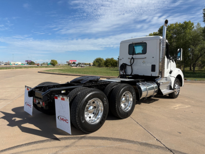 Kenworth T880 tractor rear view showing dual rear axles, chrome wheels, fuel tanks, and white cab. Mudflaps with MHC logo visible.