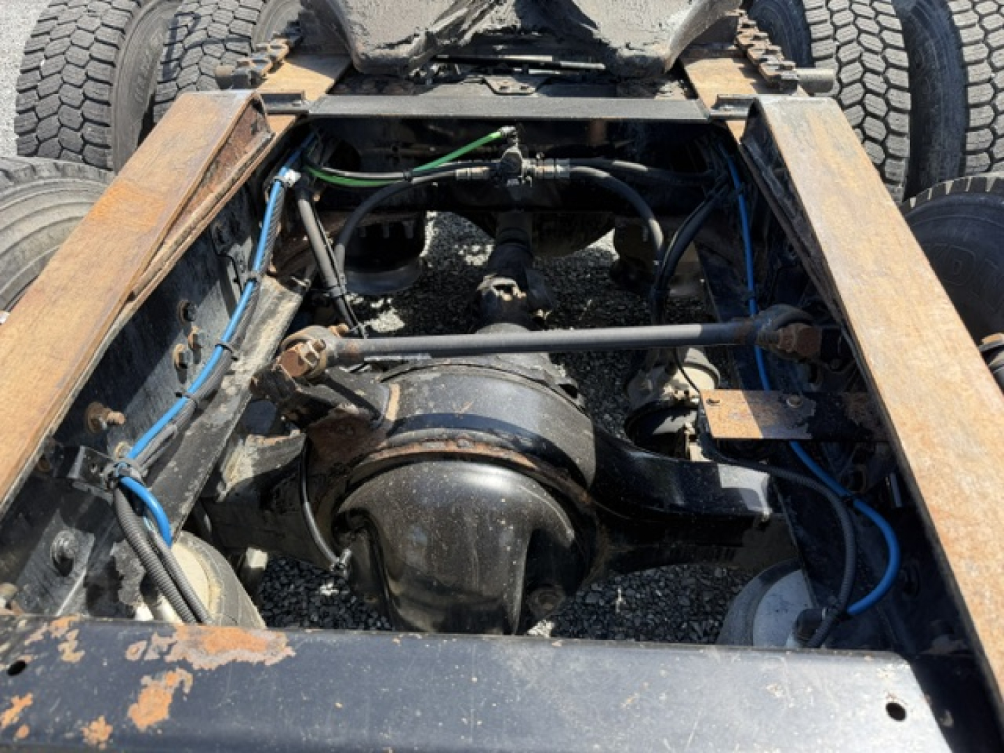 Rear engine bay view of a Freightliner Cascadia CA125DC showing driveline components, universal joints, hoses, and frame rails.