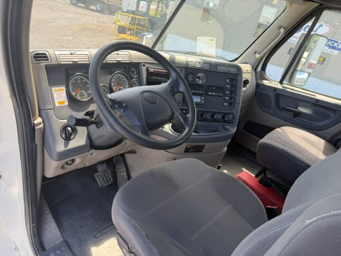 Cab interior of a Freightliner Cascadia CA125DC showing steering wheel, gauge cluster, center console, and driver seat.
