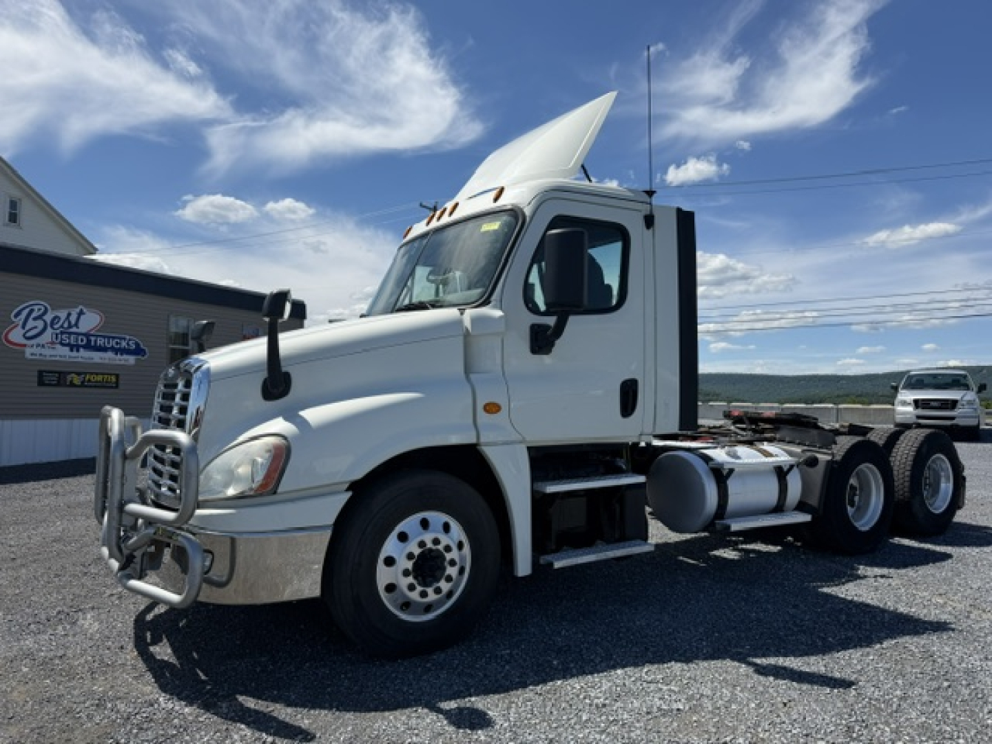 Truck cab of a 2018 Freightliner Cascadia CA125DC in a used condition, white exterior, raised sleeper with hood open, front grille guard, single rear axle configuration, daytime outdoor lot.