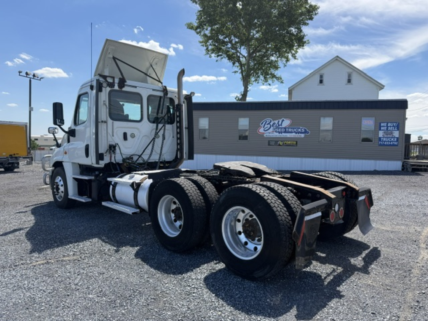 Truck chassis with dual rear axles and white cab, Freightliner Cascadia CA125DC, in a lot with a Best Used Trucks building in background.