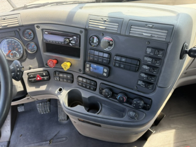 Cab interior of a 2018 Freightliner Cascadia CA125DC showing dashboard gauges, control switches, radio, cup holders, and air vent panels.