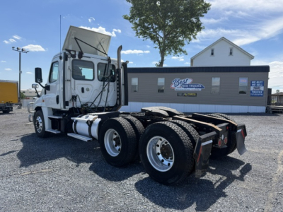 Truck chassis with dual rear axles and white cab, Freightliner Cascadia CA125DC, in a lot with a Best Used Trucks building in background.