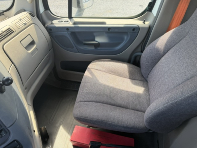 Cab interior view of a Freightliner Cascadia truck showing driver seat and door panel.