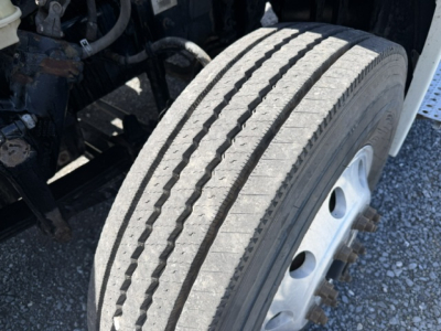 Front wheel and tire on a Freightliner Cascadia CA125DC; tread pattern visible with valve stem, part of the front axle assembly.
