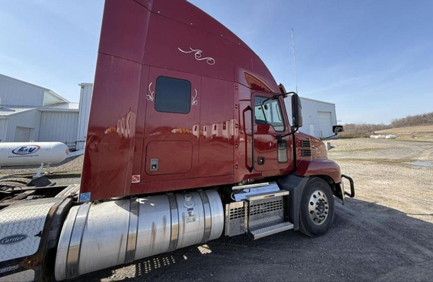 Truck cab side of a 2020 Mack Anthem conventional sleeper with maroon color, showing fuel tanks and side steps.