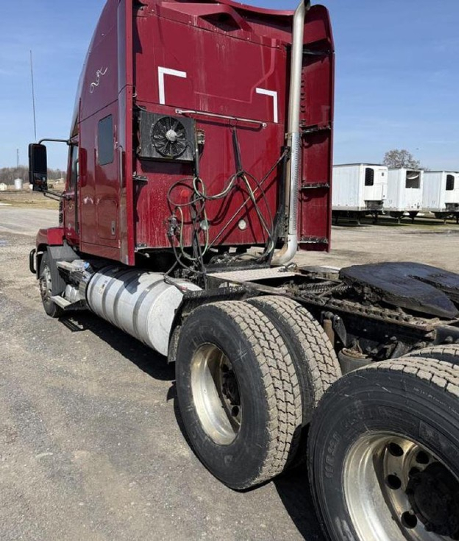 Tractor-trailer cab rear with sleeper on red Mack Anthem showing fuel tanks and dual rear wheels; exposed lines and vent on cab side.