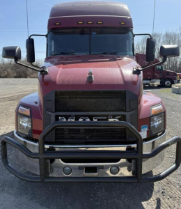 Front of red 2020 Mack Anthem sleeper cab truck with grille guard and bumper, large mirrors, black grille, and headlights visible.